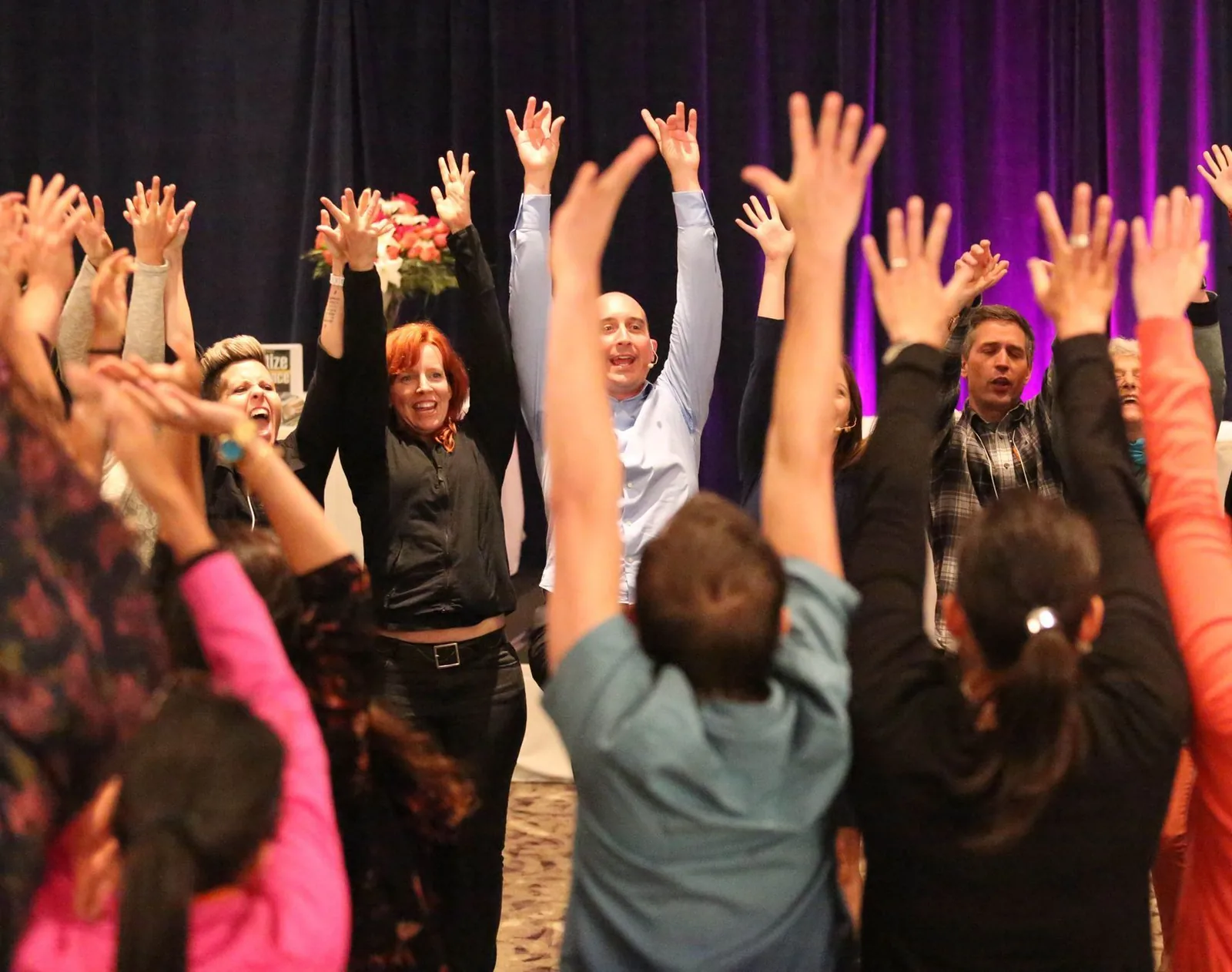 A room of workshop participants with their hands raised high, celebrating together
